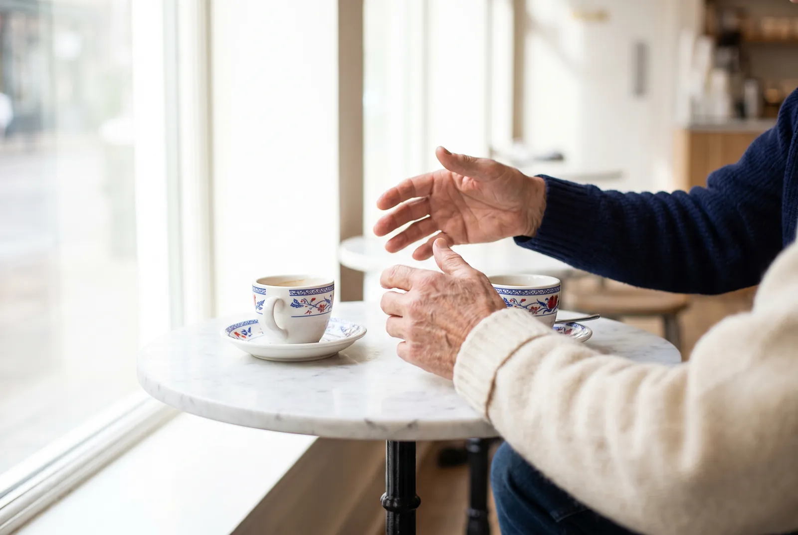 Două ceșcuțe de cafea pe o masă de marmură și mâinile a doi oameni în conversație