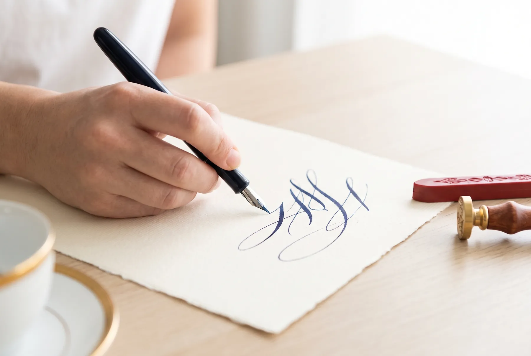 O mână scrie o scrisoare cu stiloul, lângă ceară roșie de sigiliu